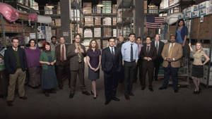 《The Office》演員站在一個有貨架盒子和美國國旗的倉庫中。 — 辦公室 壁紙