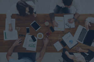 Four people working together at a wooden table with laptops and documents. — MacBook Air M3 壁紙