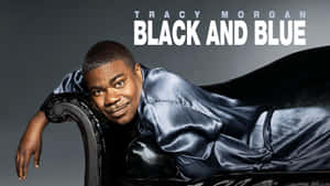Tracy Morgan 穿著黑色緞面長袍，靠在一張裝飾椅上，上面有文字疊加。 — 16:9 壁紙