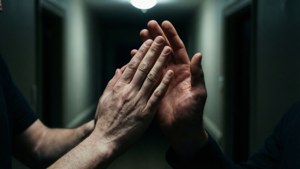 兩隻手在昏暗走廊中於單一燈光下緊握。