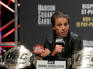 UFC拳手Joanna Jedrzejczyk在新聞發布會上發言，身旁有冠軍腰帶。 — 高清 壁紙