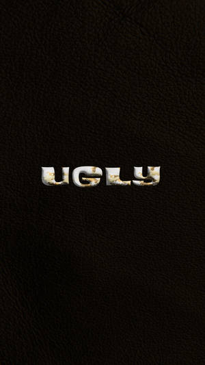 深色皮革背景上碎裂的白色字母寫著「ugly」。 — 簡約暗黑美學 壁紙