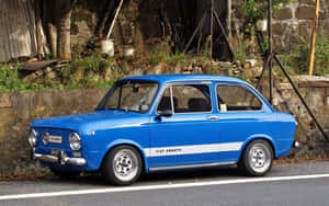 經典藍色 Fiat Abarth 停放在帶有植物的石牆旁。 — Steam Deck 壁紙