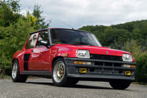 紅色雷諾5 Turbo 2跑車停泊在碎石路上，後面有綠樹和山丘。 — 雷諾 壁紙