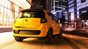 夜間停放在城市人行道上的黃色汽車，後面有亮燈的建築物。 — 飛雅特 壁紙