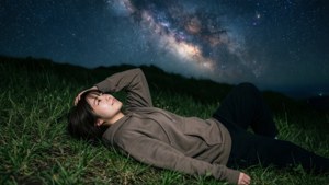 年輕女子夜晚躺在銀河系下的草地上