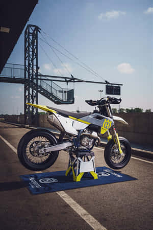 在賽車場展示的白色和黃色 Husqvarna 越野摩托車。 — iPhone Duo 壁紙
