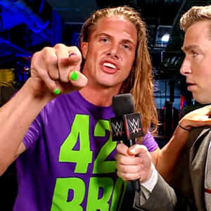 穿著紫色襯衫的WWE摔角手，綠色指甲，在採訪時指向鏡頭。 — WWE GIF 壁紙