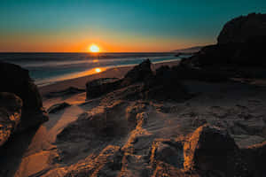 夕陽下的岩石海灘，伴隨著海浪和溫暖的金色光芒。 — 海灘日落 壁紙