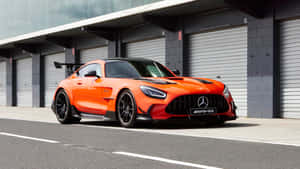 橙色 Mercedes-AMG GT R 跑車停放在工業車庫門前。 — Mercedes-Benz 壁紙