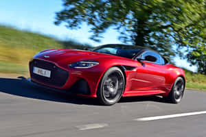 紅色Aston Martin跑車在鄉村道路上疾駛，背景有綠色樹木。 — Surface Laptop 壁紙