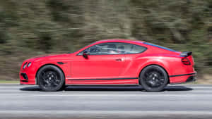 紅色賓利 Continental GT 在道路上疾馳，背景有模糊的樹木。 — 2560x1440 壁紙