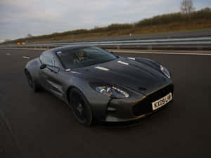 消光黑色Aston Martin V12 Vantage在高速公路上奔馳，帶有動態模糊效果。 — 奧斯頓馬丁 壁紙