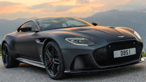 消光黑色Aston Martin DBS跑車在日落時停放在道路上，背後有山脈。 — 超跑 壁紙