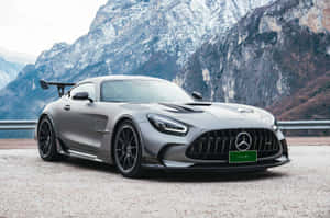 消光灰色 Mercedes-AMG GT Black Series 在山路上，後方有白雪覆蓋的山峰。 — Surface Laptop 壁紙