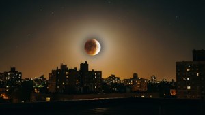 夜間城市上空的月全食，帶有明亮的窗戶和星星。