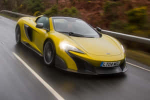 黃色McLaren跑車在潮濕的道路上行駛，背景模糊的綠色植物。 — Surface Laptop 壁紙