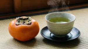 榻榻米上柿子旁邊的一杯熱氣騰騰的綠茶。