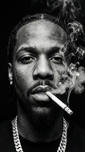 一名梳辮子的男人抽煙，煙霧在黑暗背景中升起。