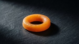 一個釉面橙色環形糖果，背景為深色石板。