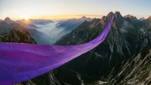紫色布料在日出時分飄揚於山巒景觀之上