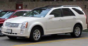 白色Cadillac SRX SUV停放在鋪砌的停車場，靠近磚牆。 — 凱迪拉克 壁紙