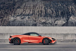 橙色McLaren跑車停在混凝土牆和岩石懸崖附近。 — Surface Pro 壁紙