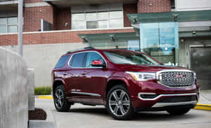 棗紅色GMC Acadia SUV停放在現代磚和玻璃建築前。 — MacBook Air M1 壁紙