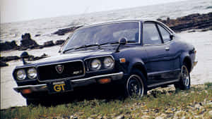 經典黑色Datsun 510 GT停泊在岩石海灘上，背景是海洋。 — 馬自達 壁紙