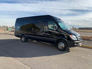 黑色 Mercedes-Benz Sprinter 客貨車停在鋪砌的停車場，遠處有工業建築和圓頂。 — Mercedes-Benz 壁紙