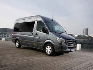 灰色 Mercedes-Benz Sprinter 客貨車停在木製屋頂上，背景有城市建築。 — Mercedes Benz C300 壁紙