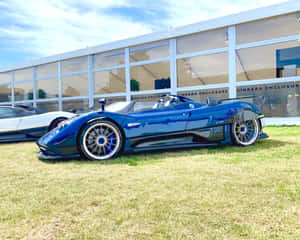 一輛藍色Pagani Zonda跑車停泊在玻璃建築附近的草地上。 — 5:4 壁紙