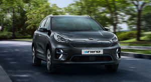 深灰色Kia e-Niro電動SUV行駛在綠樹成蔭的道路上。 — 起亞 壁紙