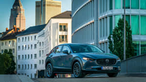 日落時分，深藍色Mazda CX-3停放在混合建築風格的城市中。 — 馬自達 壁紙