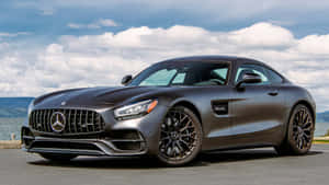 啞光灰色梅賽德斯-AMG GT跑車在雲層密佈的天空下停泊在海岸邊。 — Mercedes-Benz 壁紙