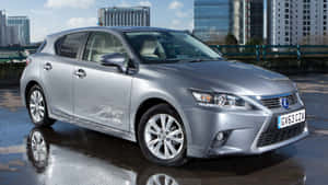 銀色Lexus CT 200h停泊在濕漉漉的路面上，背後是城市建築。 — 凌志 壁紙