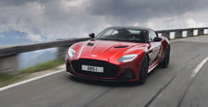 紅色Aston Martin DBS Superleggera在模糊背景的山路上飛馳。 — 奧斯頓馬丁 壁紙