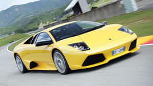 黃色藍寶堅尼 Murciélago 在賽道上飛馳，背景是山巒。 — 蘭博基尼 壁紙