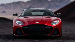 紅色Aston Martin跑車停在沙漠地形上，後面有山脈。 — 奧斯頓馬丁 壁紙