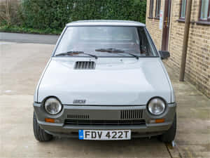 銀色復古Fiat 126停在有綠色灌木的磚造建築旁。 — 飛雅特 壁紙