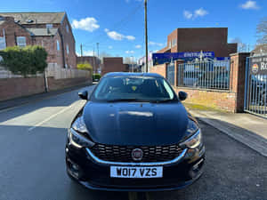 黑色Fiat Punto停泊在陽光明媚的城市街道上，靠近磚砌建築和一個閘門。 — 飛雅特 壁紙