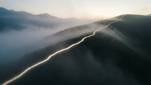 一條發光的山路在黎明時分穿過霧氣，帶著柔和的金色光芒。