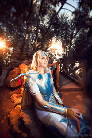 穿著藍色奇幻盔甲的cosplayer在森林的夕陽下坐在岩石上。 — 華為Pura X Max 壁紙