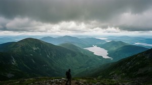 一位遠足者在山脊上俯瞰著雲層下的山谷和湖泊。