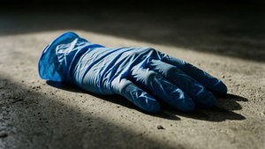 在強烈陽光下，粗糙混凝土上被丟棄的藍色醫用手套。
