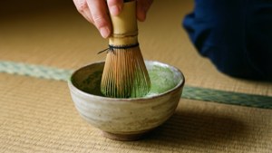手在榻榻米上的陶瓷碗中攪拌抹茶粉。