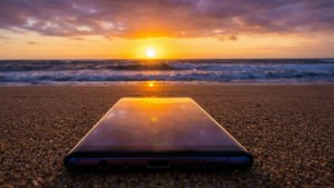 沙灘上的智慧型手機映照著夕陽在海浪之上