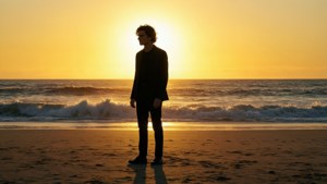 身穿深色西裝的男子獨自站在金色夕陽下的沙灘上，伴隨著海洋的波浪