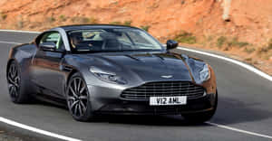 銀色Aston Martin DB11在日落時分行駛在蜿蜒的山路上。 — 奧斯頓馬丁 壁紙