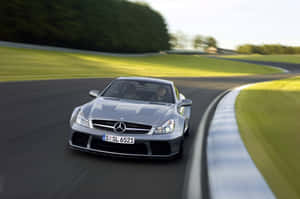 銀色 Mercedes SL65 AMG 在賽道上飛馳，周圍有綠草和樹木。 — Surface Pro 壁紙